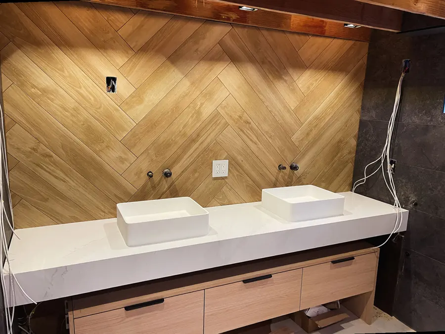 Floating double vanity cut from one slab against a herringbone wood wall